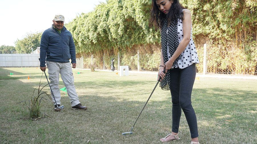 A women playing Golf while a man is looking on