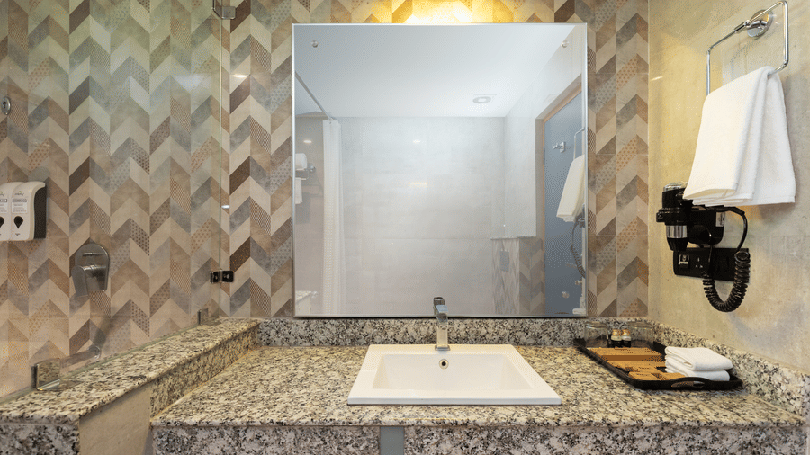 A bathroom with a white sink set in a granite countertop, a mirror with lighting above at The Golden Tusk, Jim Corbett