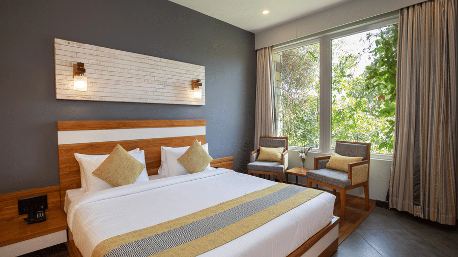 A bedroom featuring a large bed with a white headboard, a sitting area by a large window  at The Golden Tusk, Jim Corbett