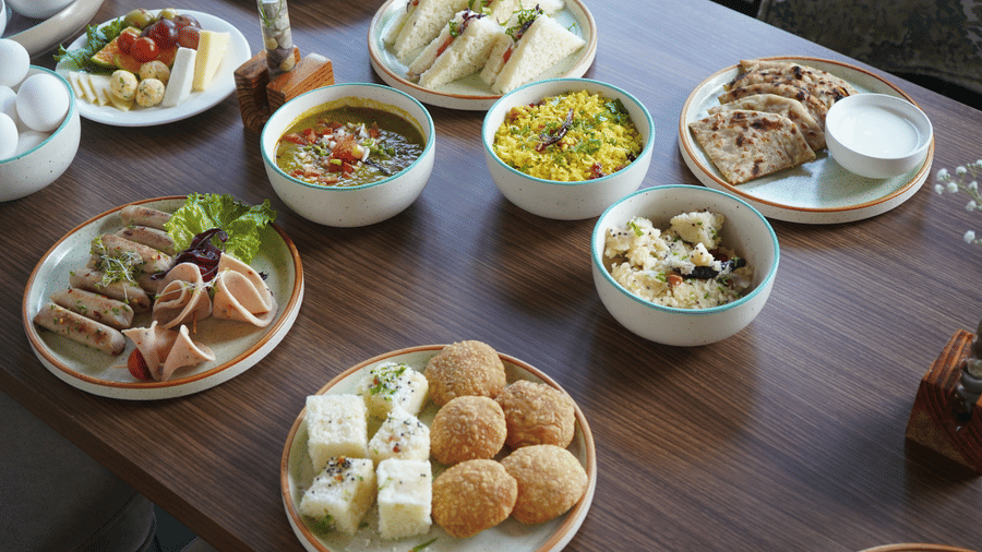 a wooden dining table laden with multiple plates and bowls containing various breakfast  at at The Golden Tusk, Jim Corbett