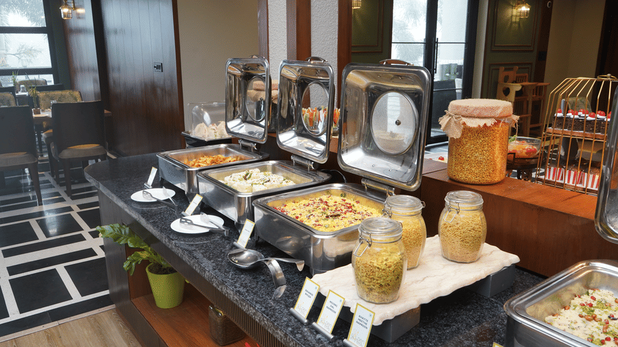 An indoor buffet setup with a long table displaying various food items in chafing dishes at The Golden Tusk, Jim Corbett