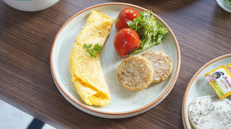 A plate with a meal including eggs, a tomato slice, and a bread on a wooden table at at The Golden Tusk, Jim Corbett