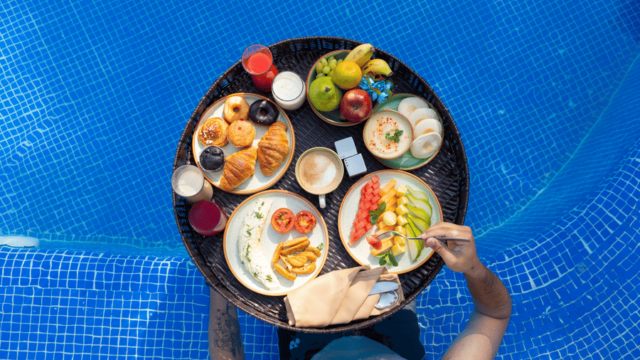 person floating  near the floating tray holding breakfast items and drinks in a blue swimming pool at The Golden Tusk, Jim Corbett