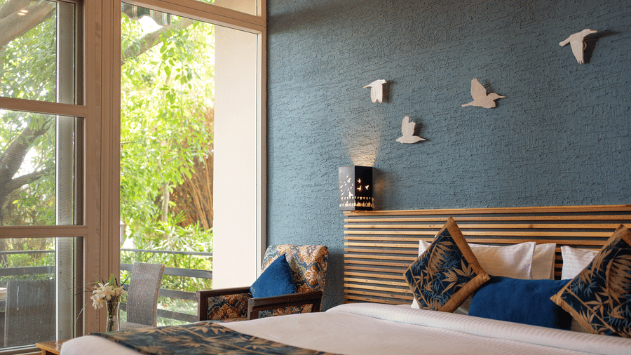 Nature View Suites with a bed, a accent wall decorated with bird decals, and a large window overlooking greenery  at The Golden Tusk, Jim Corbett