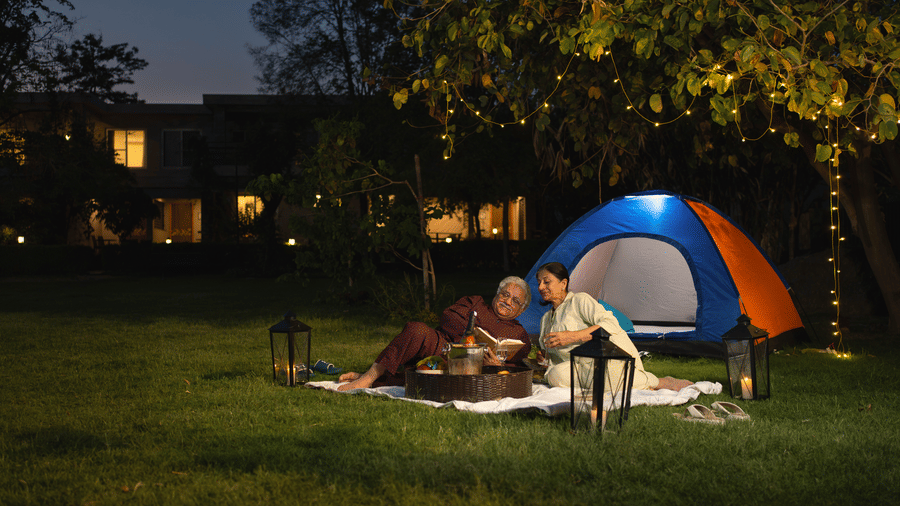 A tent pitched on grass at night, with a fire pit and people sitting around it at The Golden Tusk, Jim Corbett