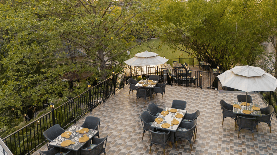 utdoor restaurant patio with multiple tables and chairs under umbrellas, surrounded by lush greenery at The Golden Tusk, Jim Corbett