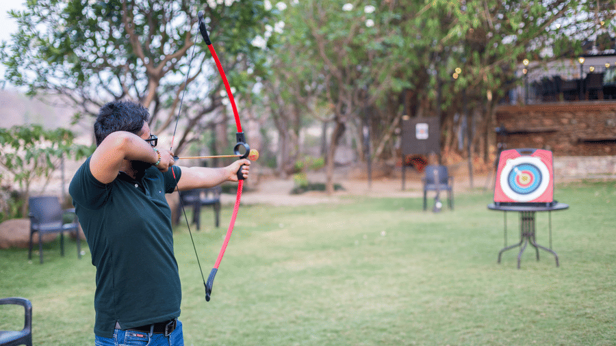 A person practicing archery outdoors, aiming a bow and arrow at a target at The Golden Tusk, Jim Corbett