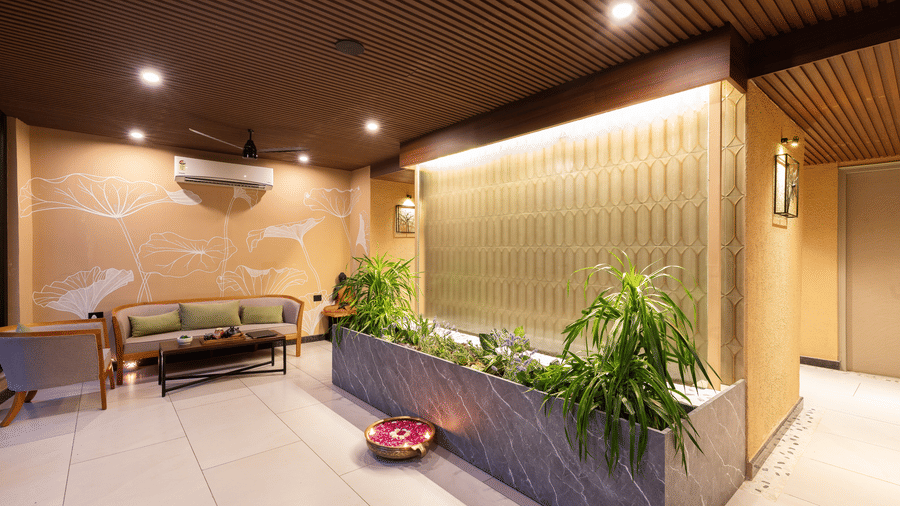 A modern, warmly lit indoor lobby area featuring a seating area, a large planter with greenery, and a decorative backlit wall feature  at The Golden Tusk, Jim Corbett