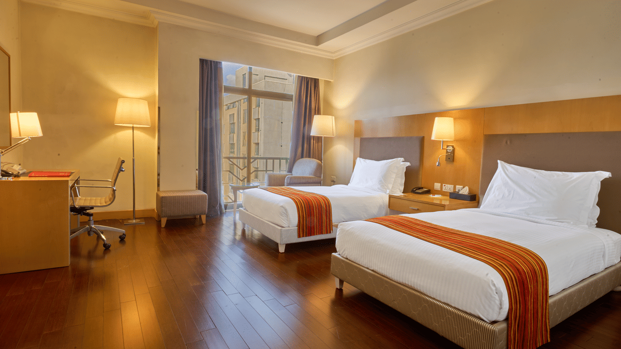 Contemporary twin room at Ramada by Wyndham Addis, Addis Ababa with warm lighting, wooden flooring, and large window for natural light.