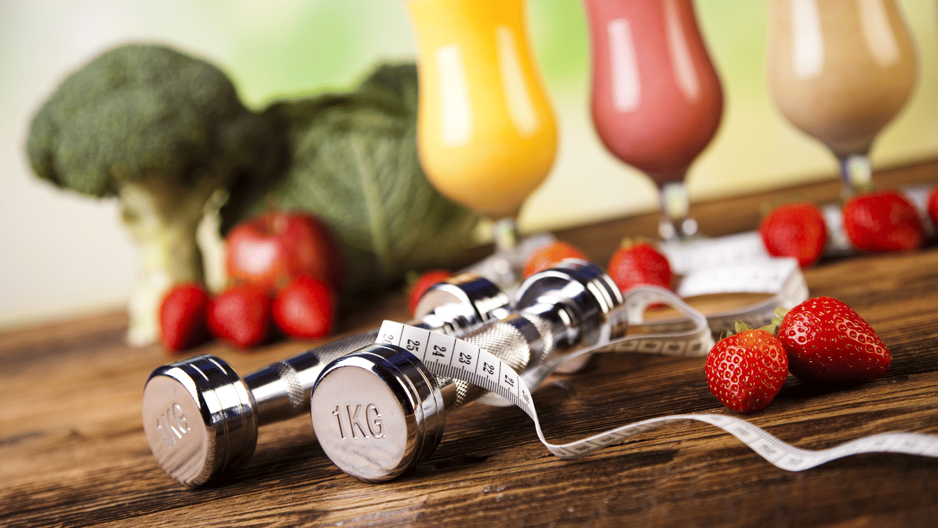 A set of 1 kilo dumbbells on a wooden surface with a set of vegetables and glasses of juices in the background