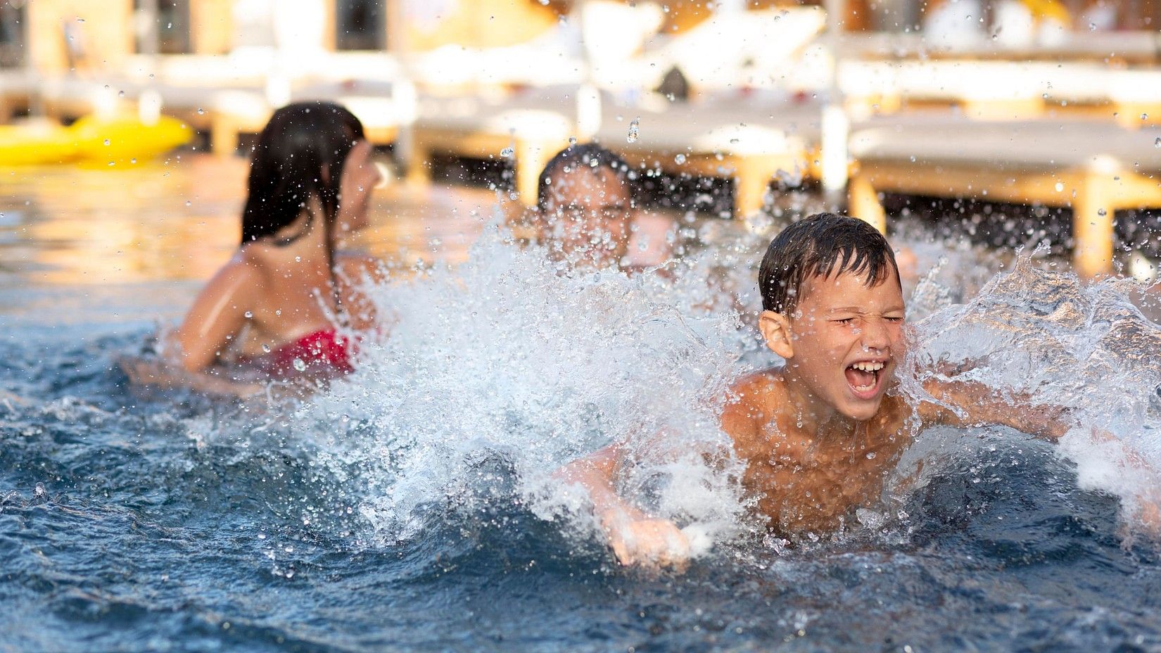 Children joyfully splashing and playing together in a swimming pool at a resort.