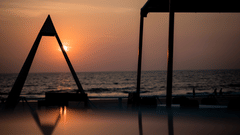 unset over the ocean with silhouetted beach structures and reflections on wet sand.
