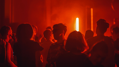a group of people standing in a club with red neon light lighting up the room