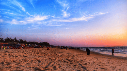A wide-angle shot of a beach shore during the sunset featuring pink and orange hues on over the crashing waves.