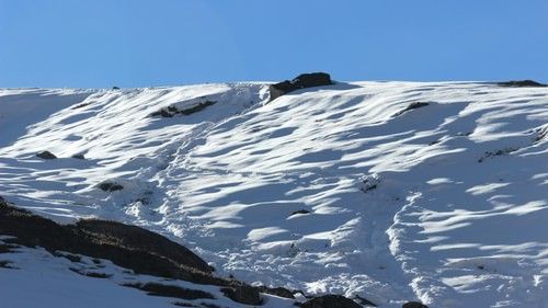 A snow-covered hillside with distinct wind patterns etched into the snow