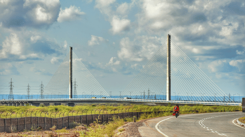 A long, modern cable-stayed bridge with two tall towers spanning over a road and landscape.