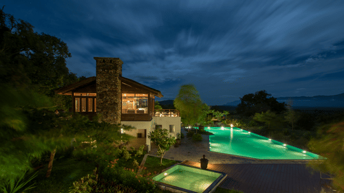 An overview of the swimming pool with the lights on as seen during twilight hour at The Serai Bandipur.