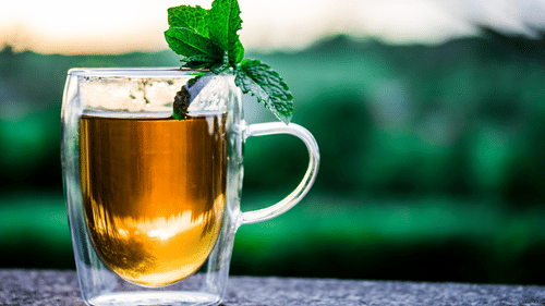 A close up shot of a glass of tea with mint leaves on it kept on a ledge.