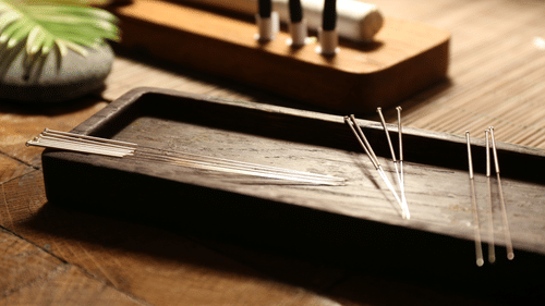 Acupuncture needles laid out on a wooden tray, with moxa sticks visible in the background