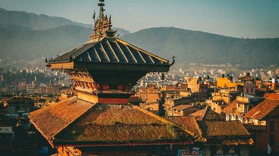 A multi-tiered pagoda roof with intricate details overlooking a cityscape and distant hills.