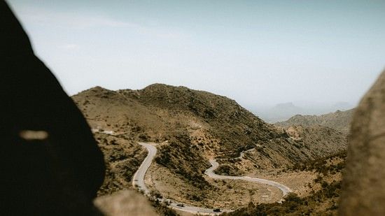 A winding road through a mountainous landscape, viewed from a rocky vantage point.