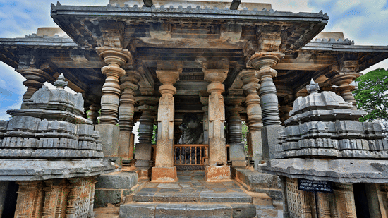 Facade view of the Nandi Pavilion of Hoysaleswara Temple with stone pillars and small buildings near the entrances on either side.