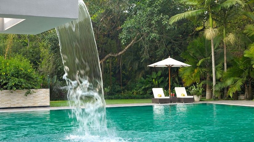 Swimming pool with a waterfall feature surrounded by lush greenery.