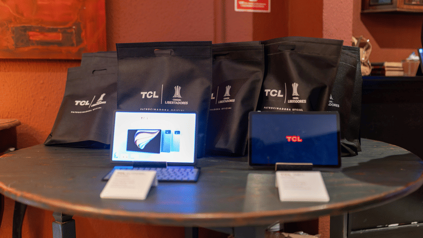 2 tablets and several black branded gift bags arranged on a wooden circular table in a warm, indoor setting.