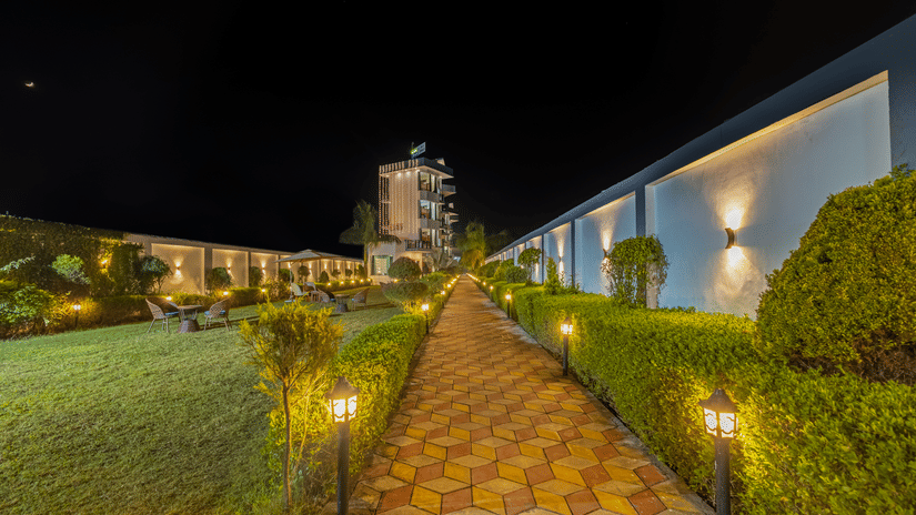 A illuminated stone pathway at night leading through manicured green lawns and garden hedges toward a distant building - Nature Trails Rishikesh