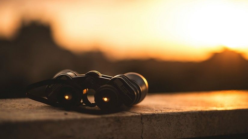 a close up shot of a binocular kept on a table with the setting sun in the background