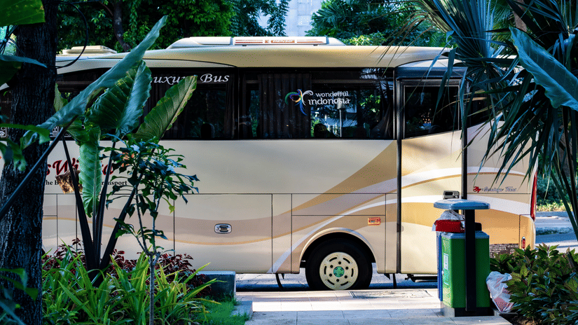 Beige shuttle bus parked outside a tropical property, framed by lush palm trees and greenery.