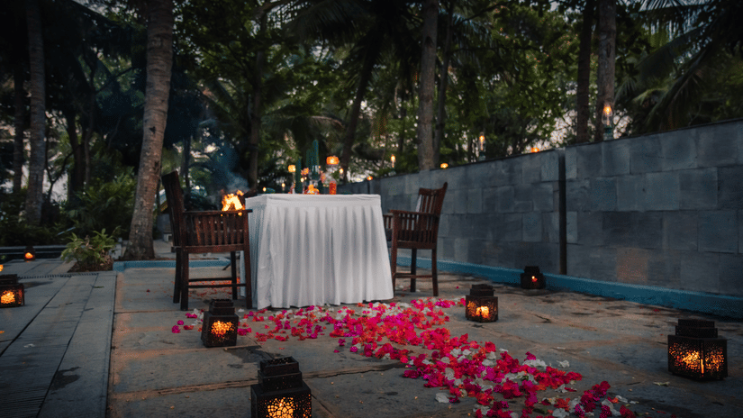 A romantic dinner setup with candles and petals on the ground.