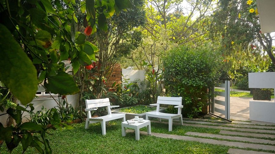 White outdoor seating arrangement in a garden with lush plants and a walking path at Amanvana Spa Resort, Coorg - Luxury Resort