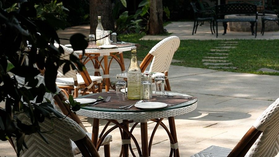 Outdoor cafe setting with wine glasses and a bottle on a table, foliage in the foreground.