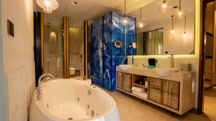 A bathroom with a modern white bathtub, gold-framed mirrors, and striking blue tiled walls that reflect the light.