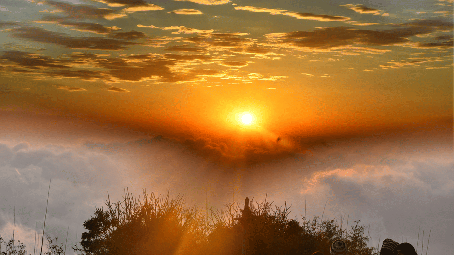 Golden sunrise above clouds at Tiger Hill with warm light spreading across the Himalayan horizon.