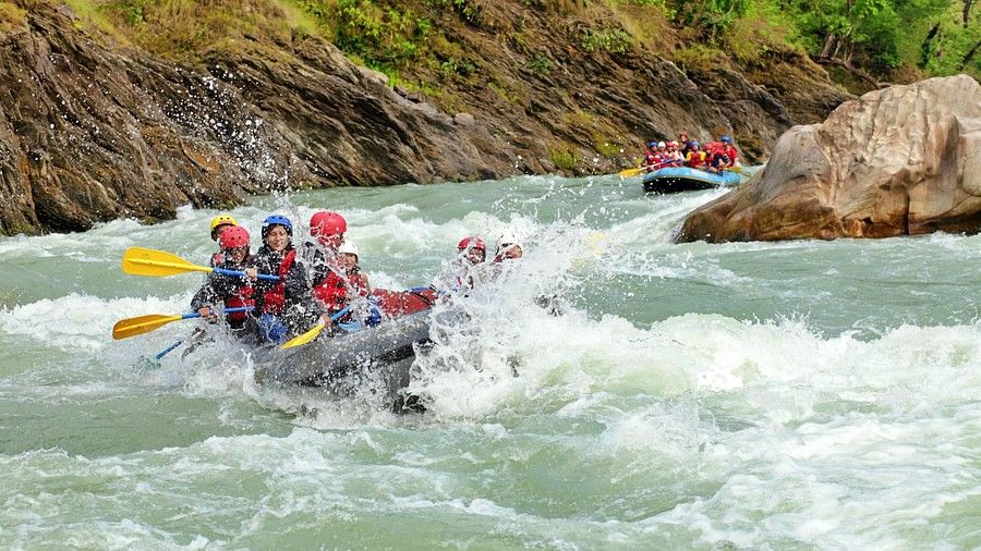 A group of people wearing red life jackets and helmets rafting down a fast-moving river surrounded by lush, green hills.