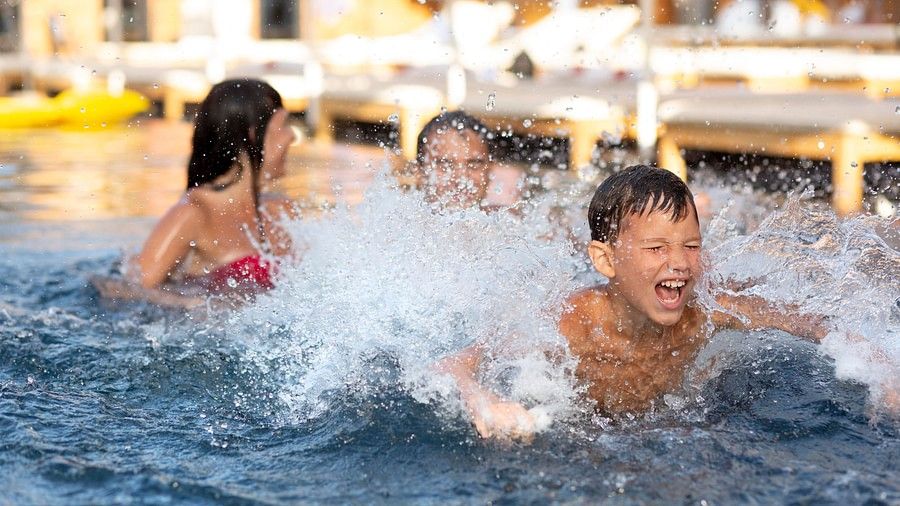 Children joyfully splashing and playing together in a swimming pool at a resort.