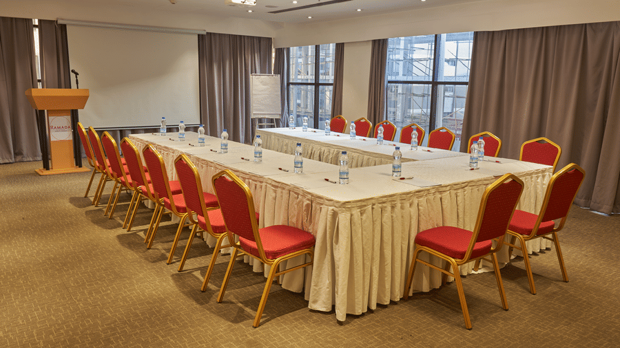 Conference room with red chairs arranged around rectangular table, warm lighting, and professional setup for meetings  - Ramada by Wyndham Addis