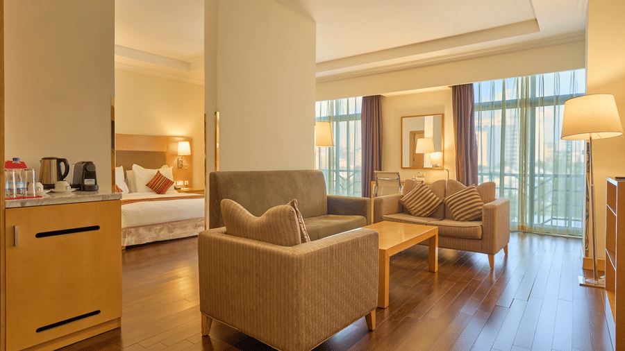 A spacious living area with sofas, coffee table, kitchenette, and large windows allowing natural light  - Ramada by Wyndham Addis
