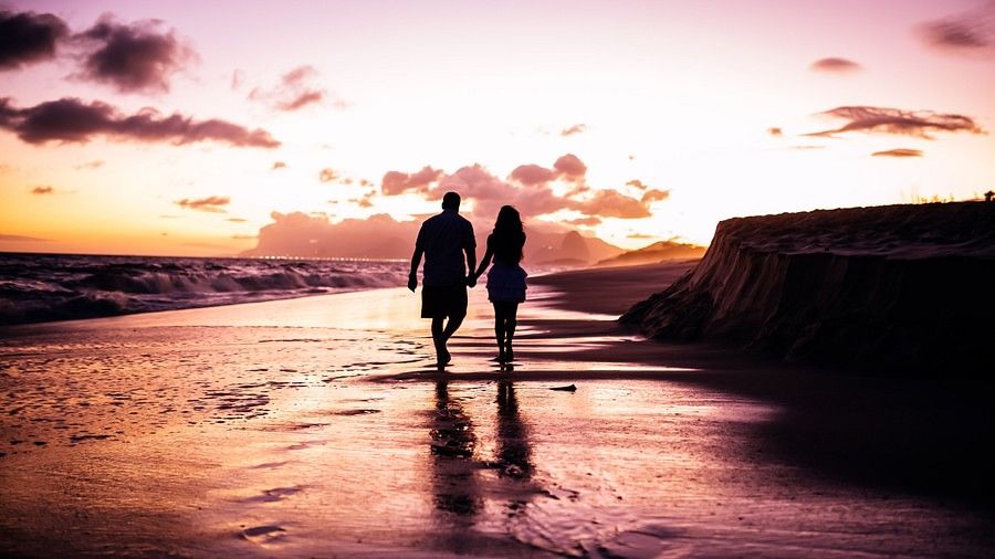 valentine day special in mumbai - a couple holding hands and walking on a sea beaching during sunset
