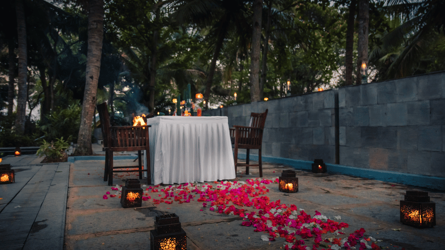 A romantic dinner setup with candles and petals on the ground.