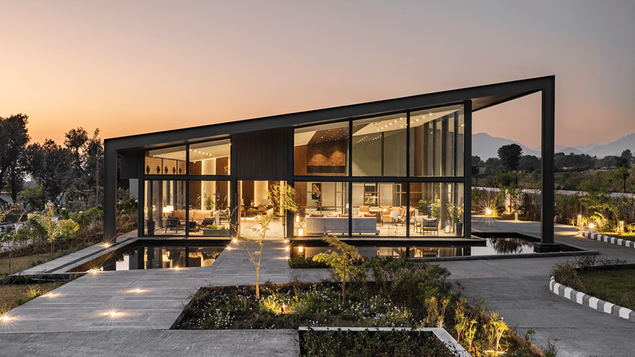The contemporary slanted-roof building at Vandhara Sarovar Premiere, Patkote, reflected in a still water feature.
