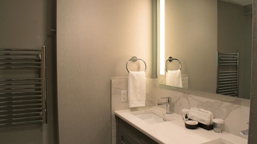 A bathroom at YO1 Longevity & Health Resorts under warm lighting featuring a large mirror and towels along with toiletries by the sink
