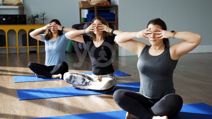 Three women sit cross-legged on blue yoga mats, covering their eyes with their hands at at YO1 Longevity & Health Resorts
