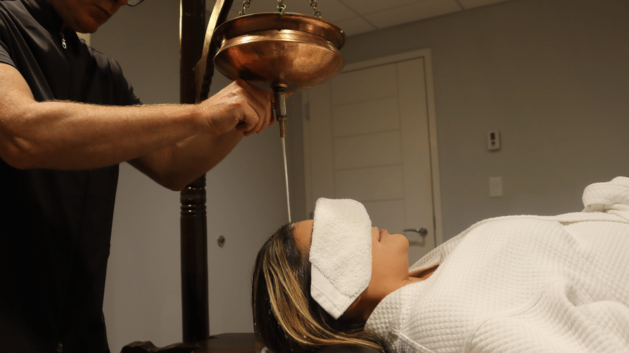 A guest at YO1 Longevity and Health Resorts in the Catskills receives a traditional Shirodhara Ayurvedic treatment where warm medicated oil is poured in a continuous and rhythmic stream onto the forehead to induce deep relaxation and mental clarity.