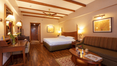 A bedroom at The Carlton featuring a bed, work desk and chair, lamps, seating area with sofa and a flat TV screen, one of the cosiest Kodaikanal rooms.