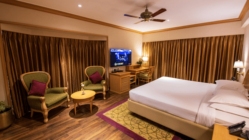 A room with a double bed, wooden furniture seating area with green & brown accents at The Clarton. One of the finest Kodaikanal rooms near lake.