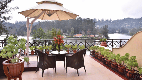 Outdoor dining area with a canopy and chairs featuring the views of pine trees and hills at the backdrop at The Carlton, Kodaikanal.