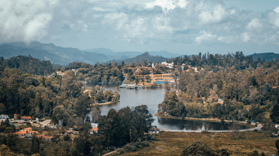 Wide view of a lake encircled by trees and residential buildings, with rolling hills stretching into the distance in Kodaikanal, Tamil Nadu.